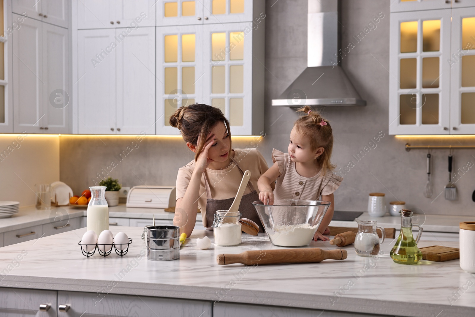 Photo of Tired housewife cooking with her little daughter at marble table in kitchen