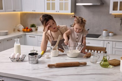 Tired housewife cooking with her little daughter at marble table in kitchen