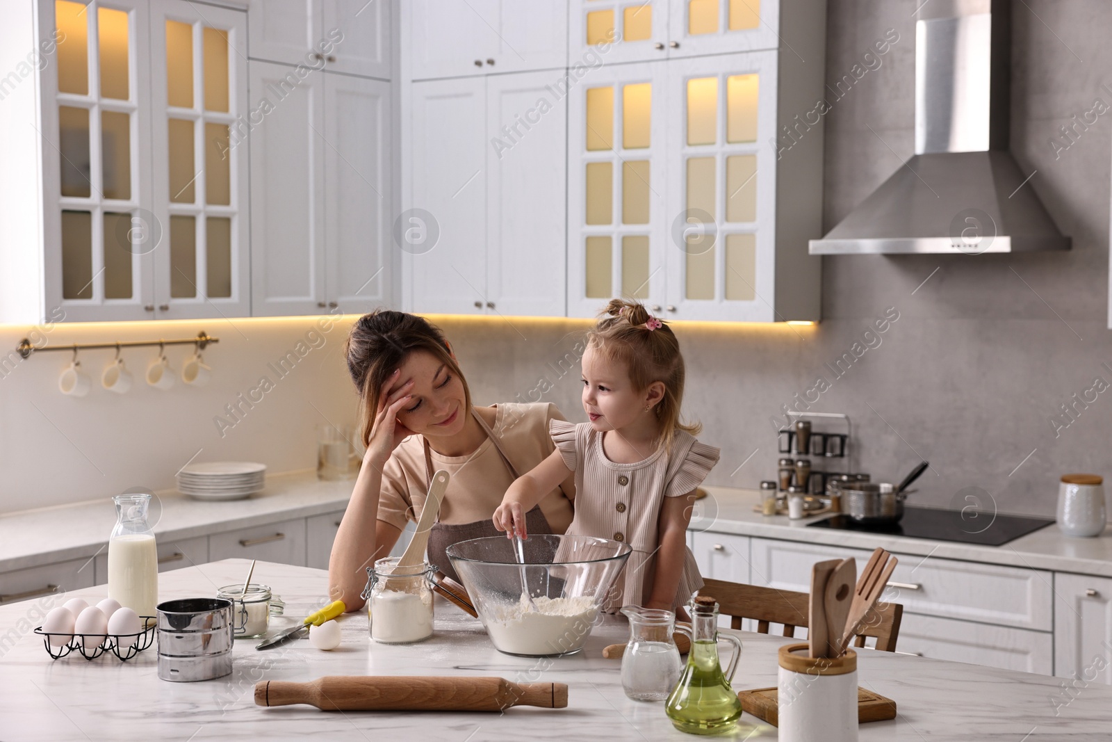 Photo of Tired housewife cooking with her little daughter at marble table in kitchen