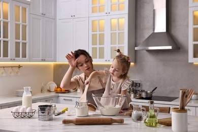 Photo of Tired housewife cooking with her little daughter at marble table in kitchen