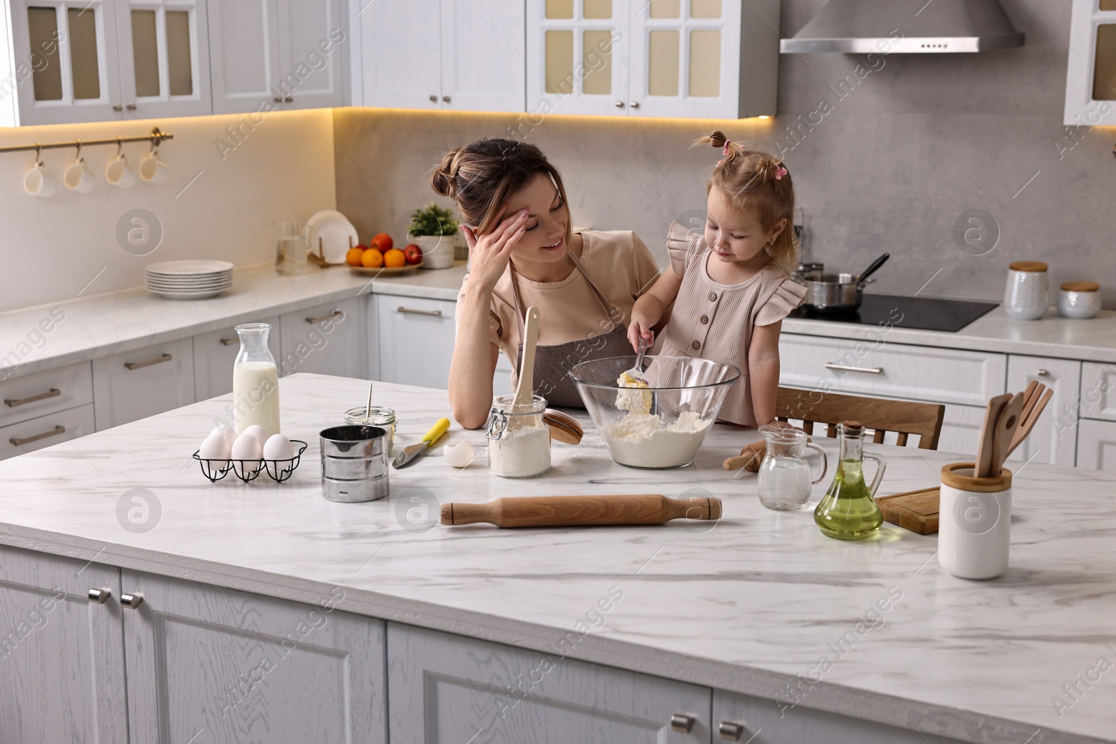 Photo of Smiling housewife cooking with her little daughter at marble countertop in kitchen