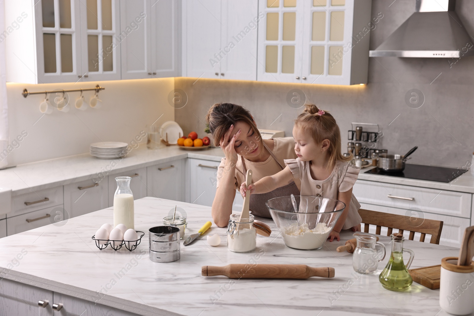 Photo of Tired housewife cooking with her little daughter at marble countertop in kitchen