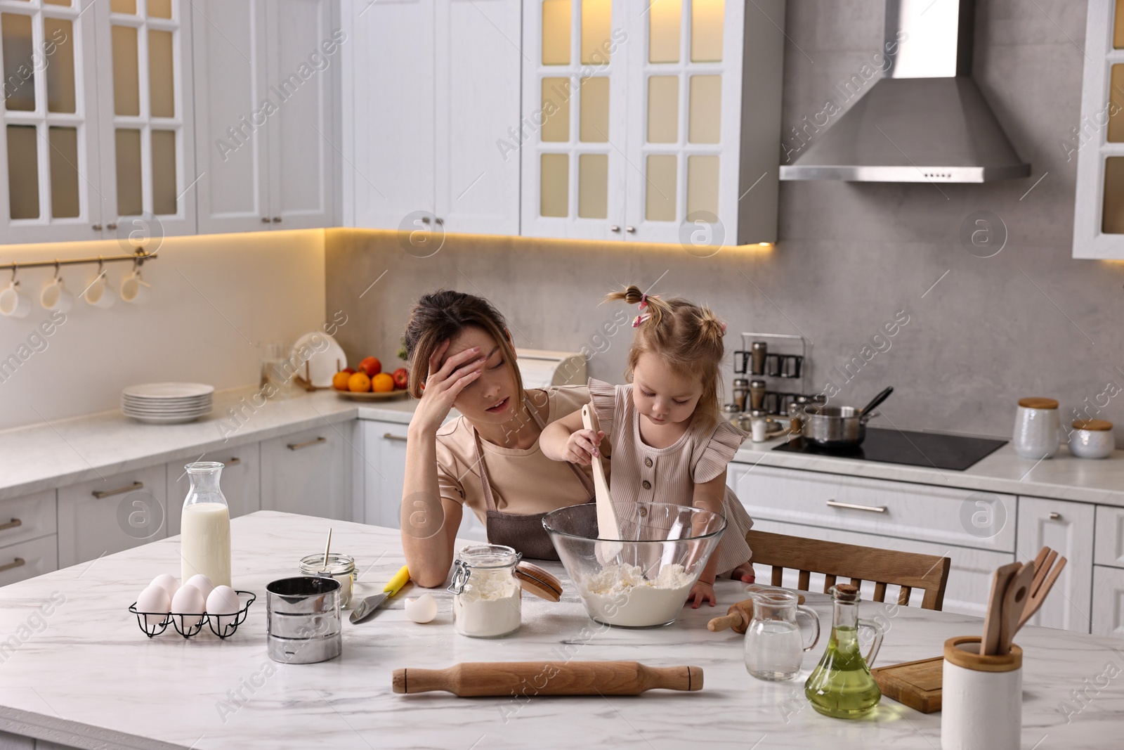 Photo of Tired housewife cooking with her little daughter at marble table in kitchen