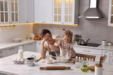 Photo of Tired housewife cooking with her little daughter at marble table in kitchen