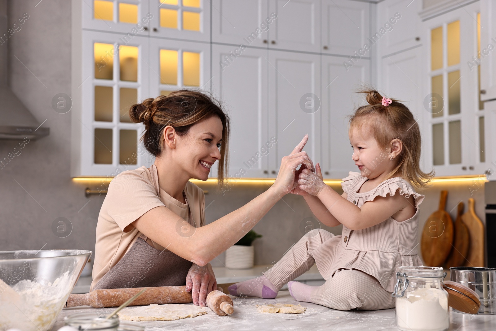 Photo of Smiling housewife cooking with her little daughter at marble table in kitchen