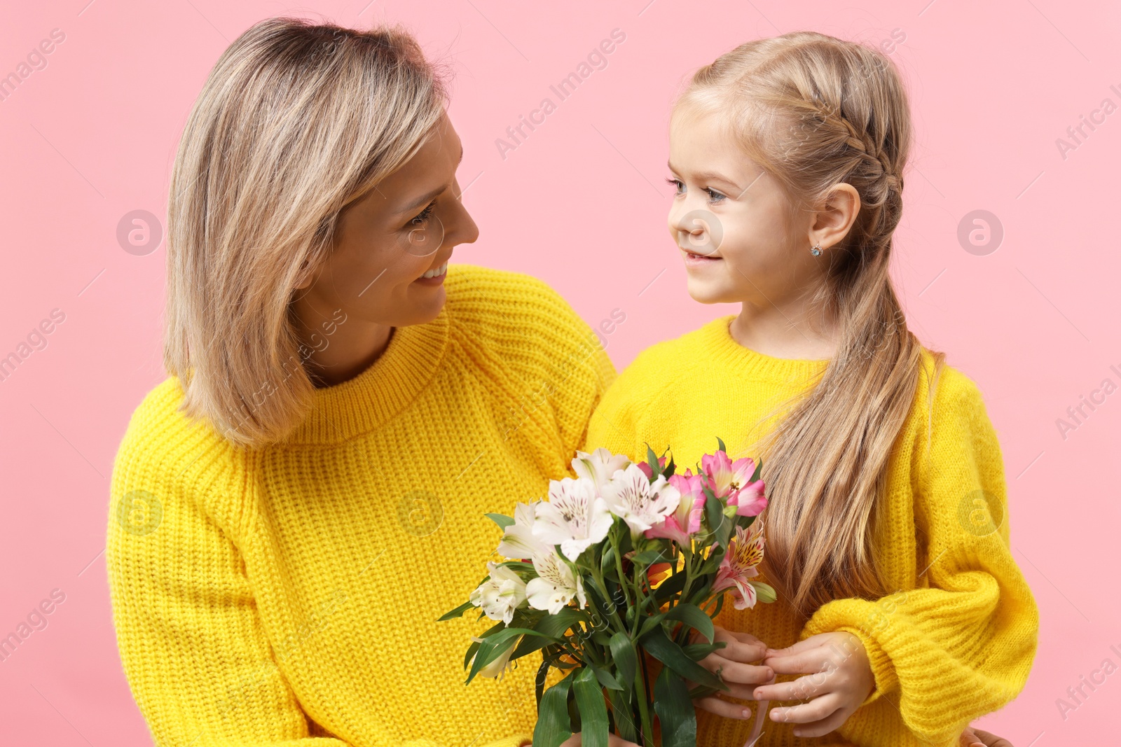 Photo of Little daughter congratulating her mom with bouquet of alstroemeria flowers on pink background. Happy Mother's Day