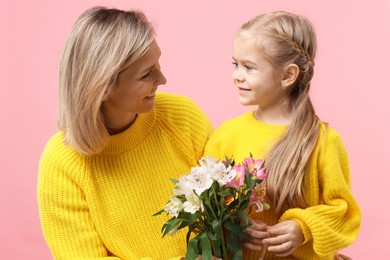 Photo of Little daughter congratulating her mom with bouquet of alstroemeria flowers on pink background. Happy Mother's Day