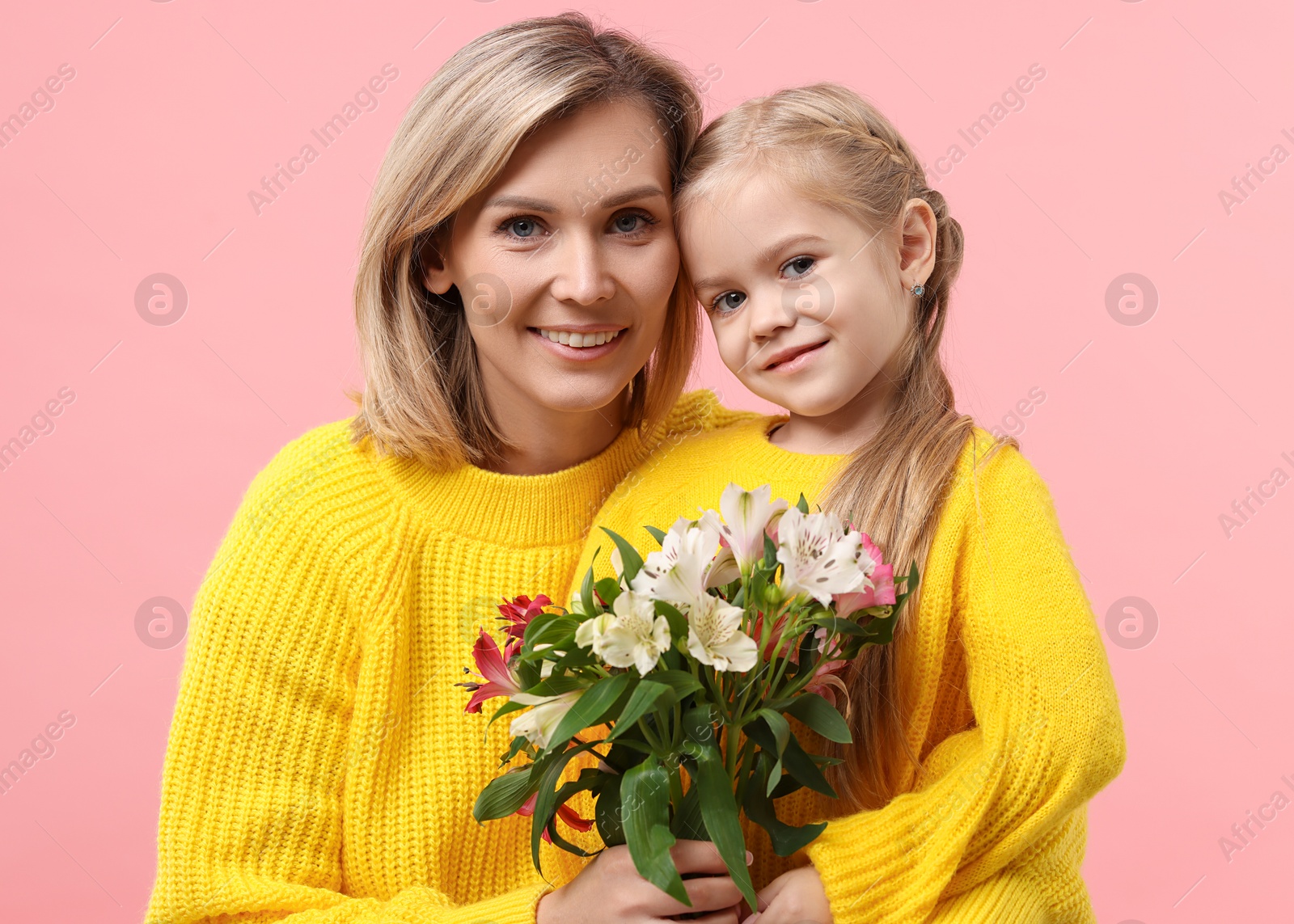 Photo of Happy woman with her daughter and bouquet of alstroemeria flowers on pink background. Mother's Day celebration