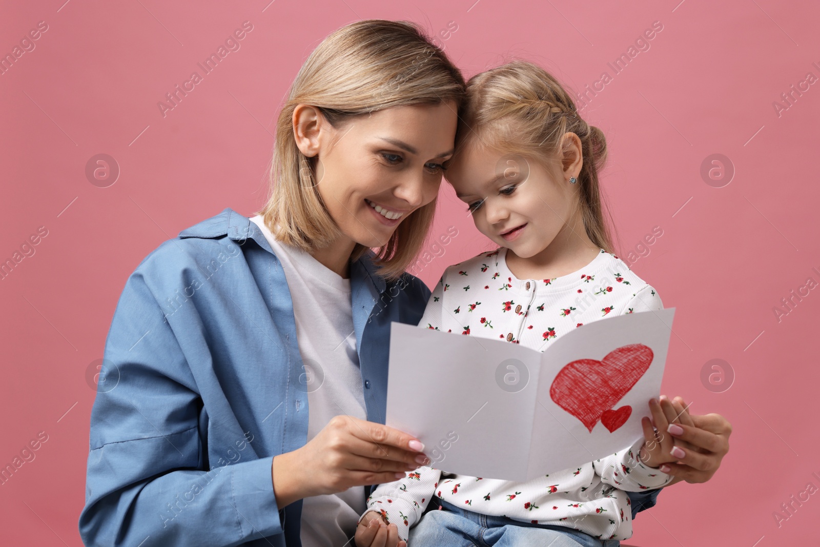 Photo of Happy woman with her daughter and greeting card on pink background. Mother's Day celebration