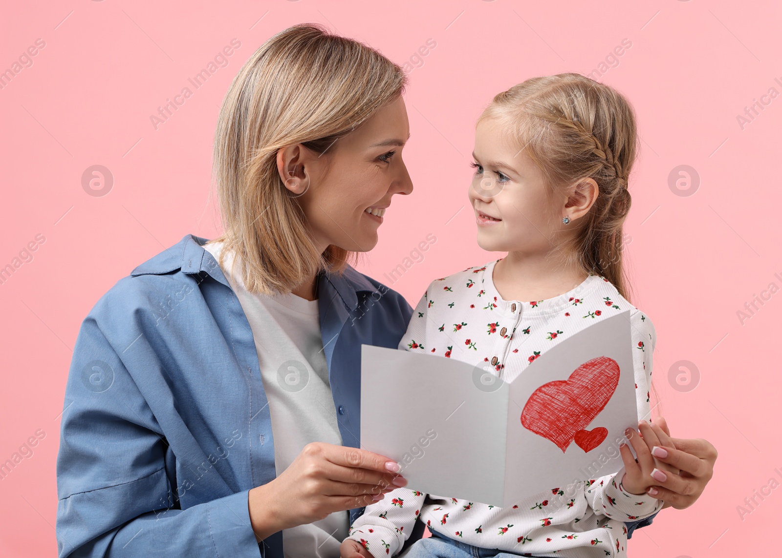 Photo of Happy woman with her daughter and greeting card on pink background. Mother's Day celebration