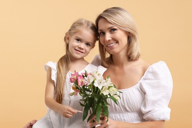 Photo of Happy woman with her daughter and bouquet of alstroemeria flowers on beige background. Mother's Day celebration