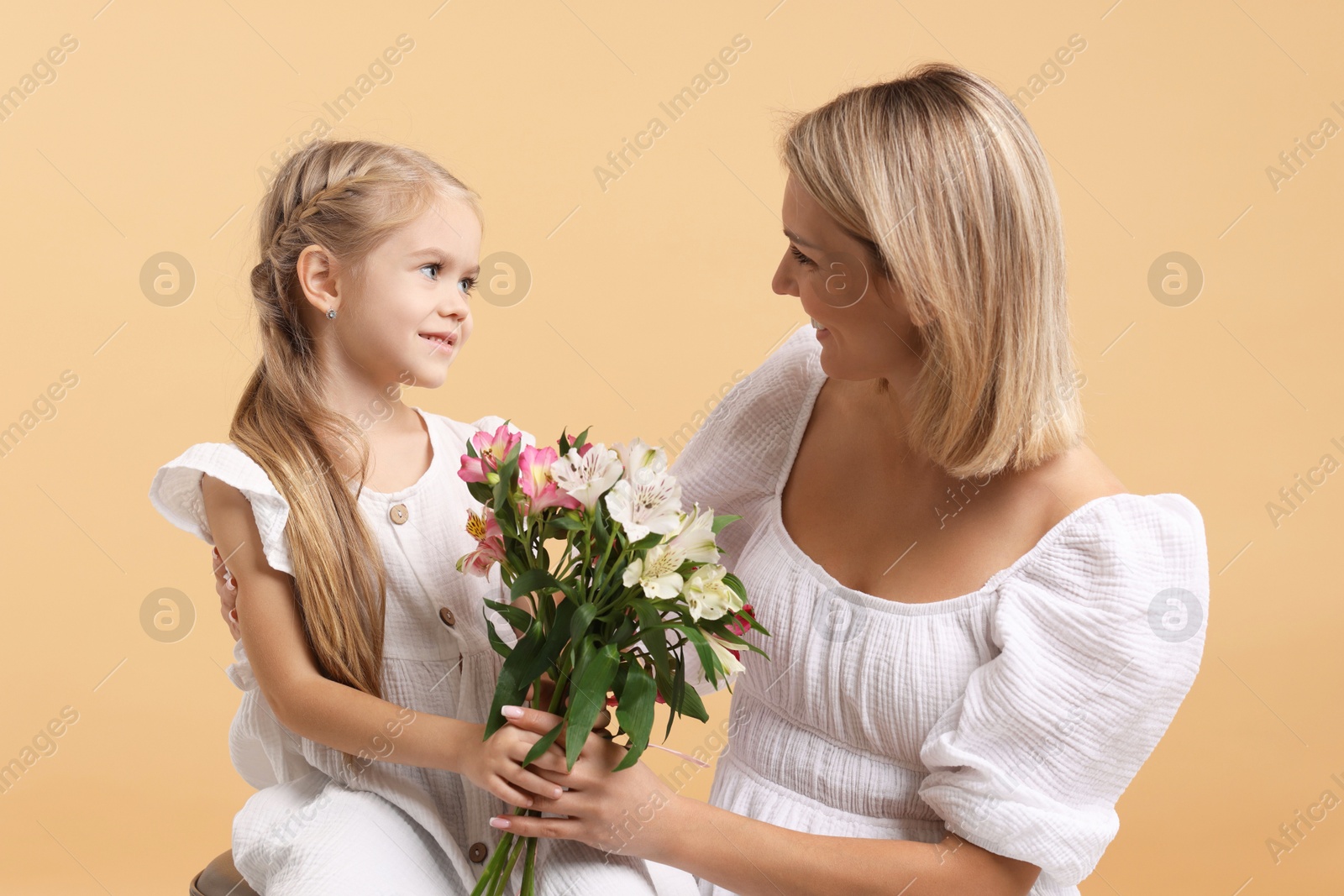 Photo of Little daughter congratulating her mom with bouquet of alstroemeria flowers on beige background. Happy Mother's Day