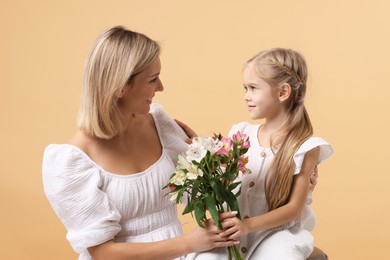 Photo of Little daughter congratulating her mom with bouquet of alstroemeria flowers on beige background. Happy Mother's Day