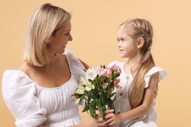 Photo of Little daughter congratulating her mom with bouquet of alstroemeria flowers on beige background. Happy Mother's Day