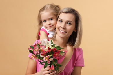 Photo of Little daughter congratulating her mom with bouquet of alstroemeria flowers on beige background. Happy Mother's Day