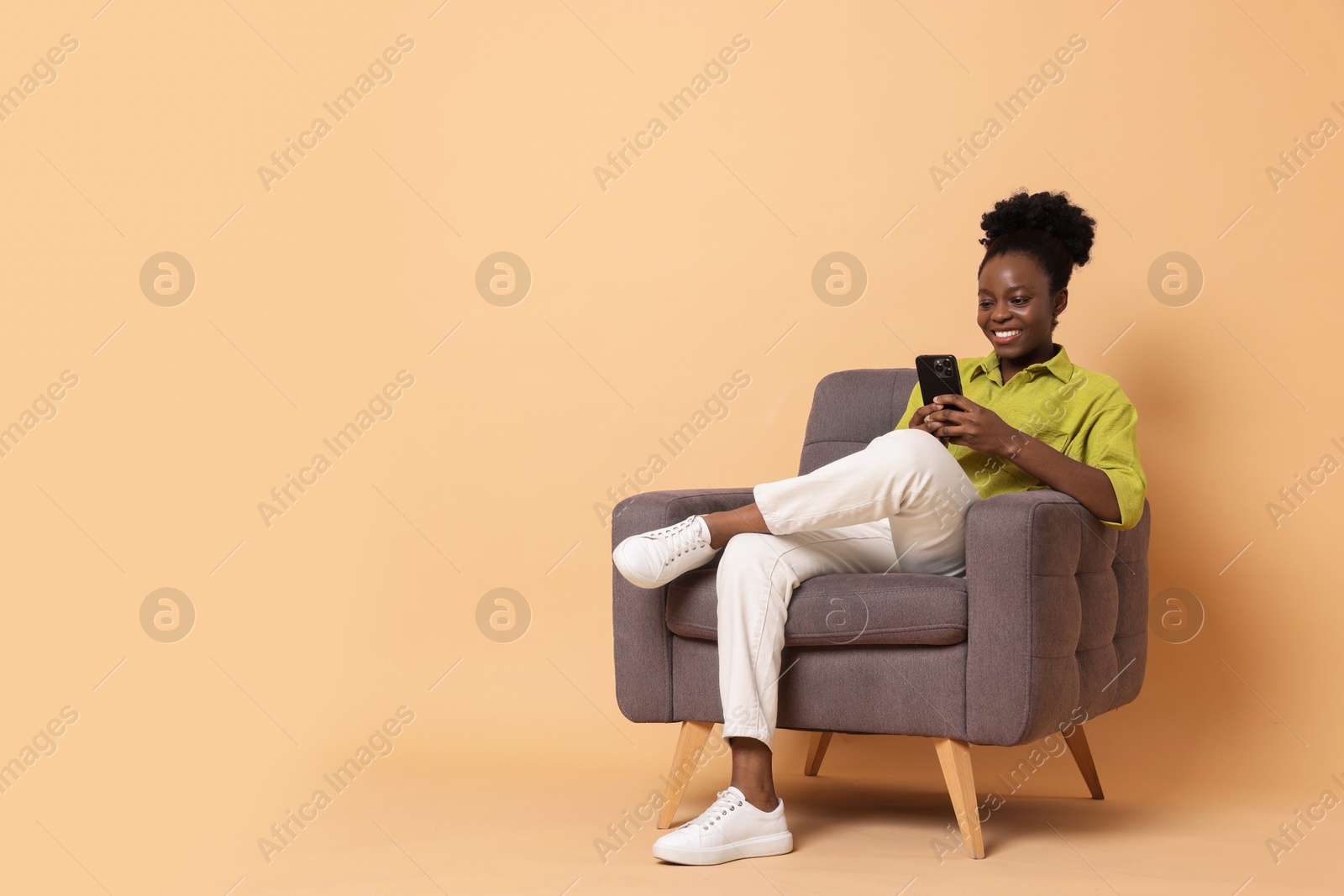 Photo of Smiling woman with smartphone sitting in armchair on beige background. Space for text