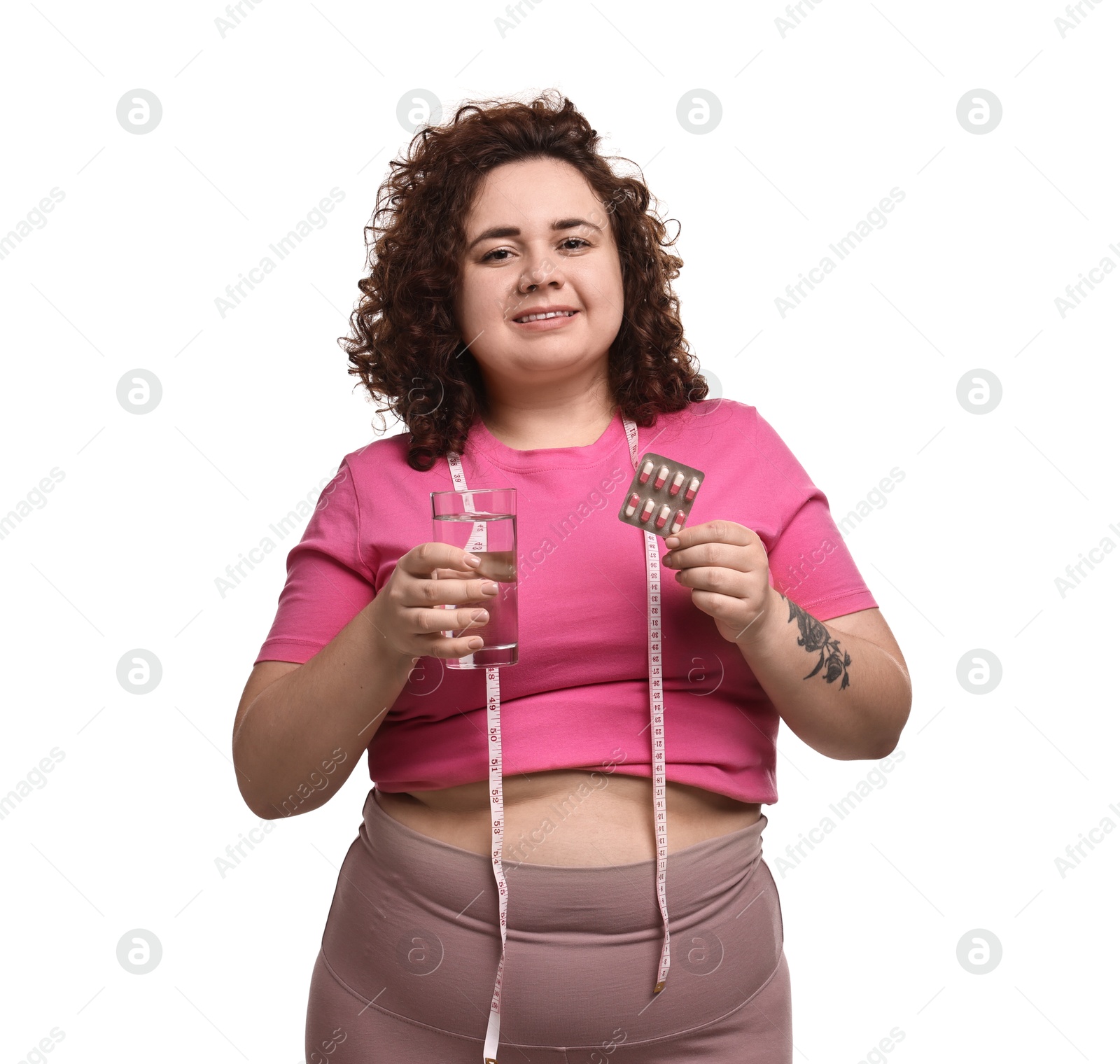 Photo of Happy plus size woman holding blister of weight loss supplements and glass of water on white background