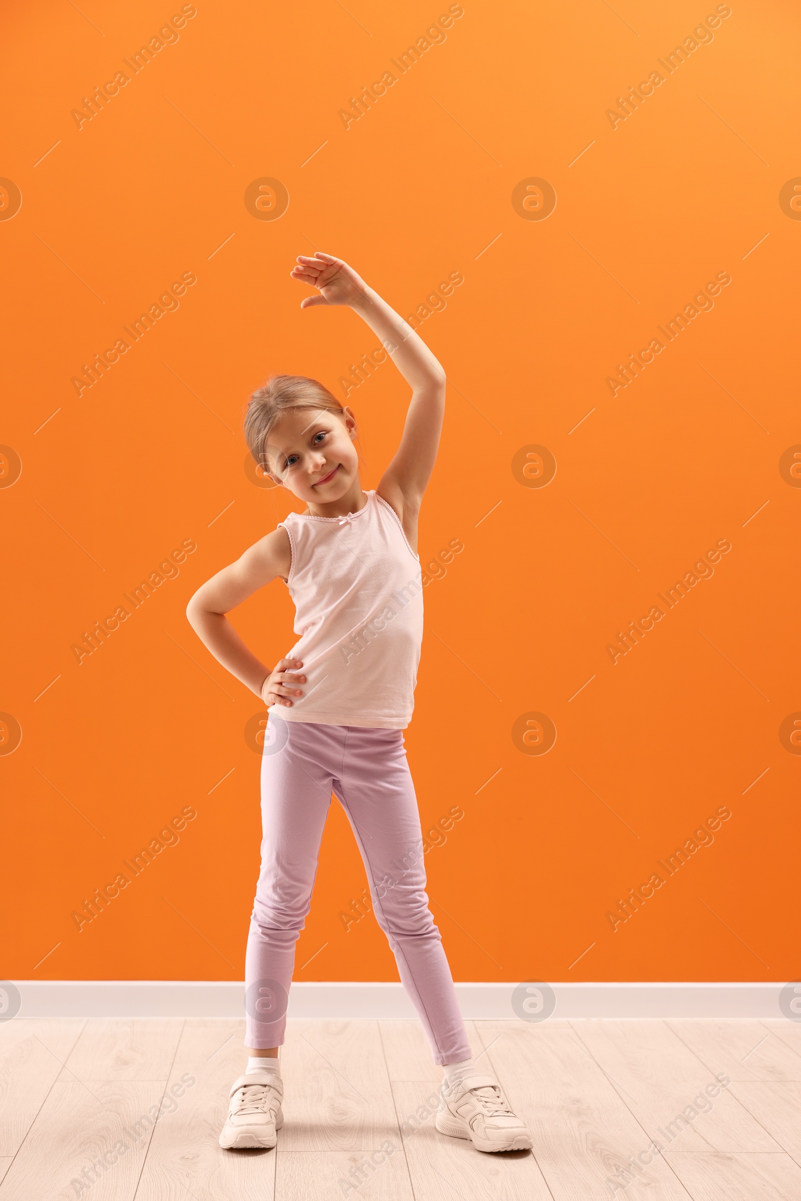 Photo of Cute little girl exercising on orange background