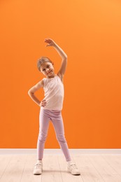 Photo of Cute little girl exercising on orange background