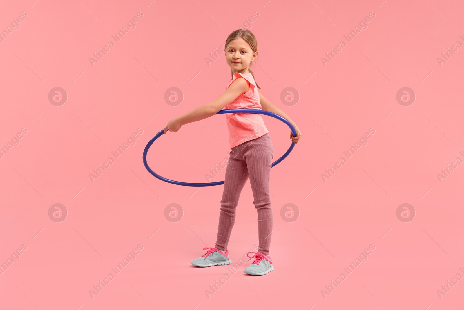 Photo of Cute little girl exercising with hula hoop on pink background