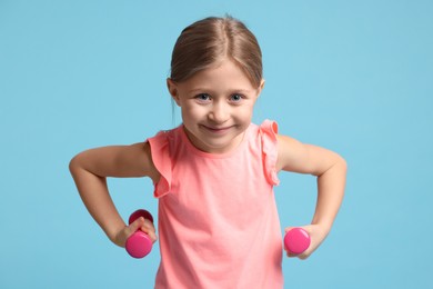 Photo of Cute little girl exercising with dumbbells on light blue background