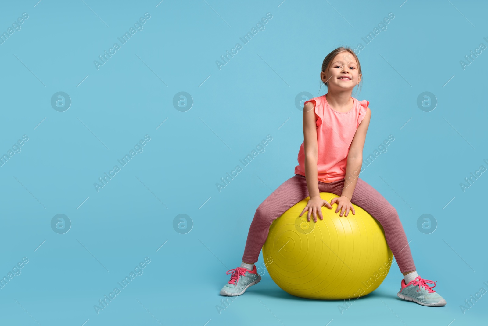 Photo of Cute little girl with fitness ball on light blue background, space for text