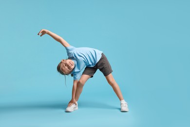 Photo of Cute little girl exercising on light blue background