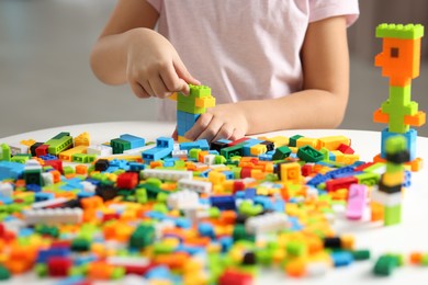 Photo of Girl playing with building blocks at white table indoors, closeup