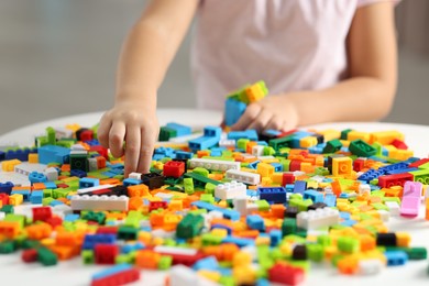 Photo of Girl playing with building blocks at white table indoors, closeup