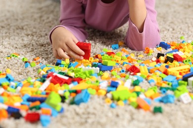 Photo of Girl playing with building blocks on floor at home, closeup