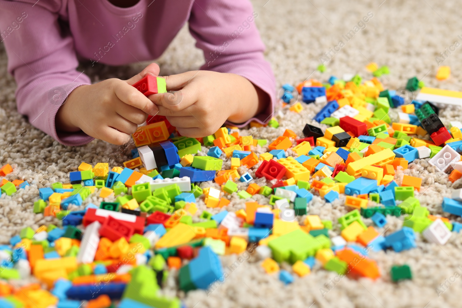 Photo of Girl playing with building blocks on floor at home, closeup