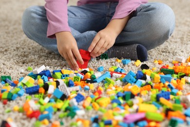 Photo of Girl playing with building blocks on floor at home, closeup