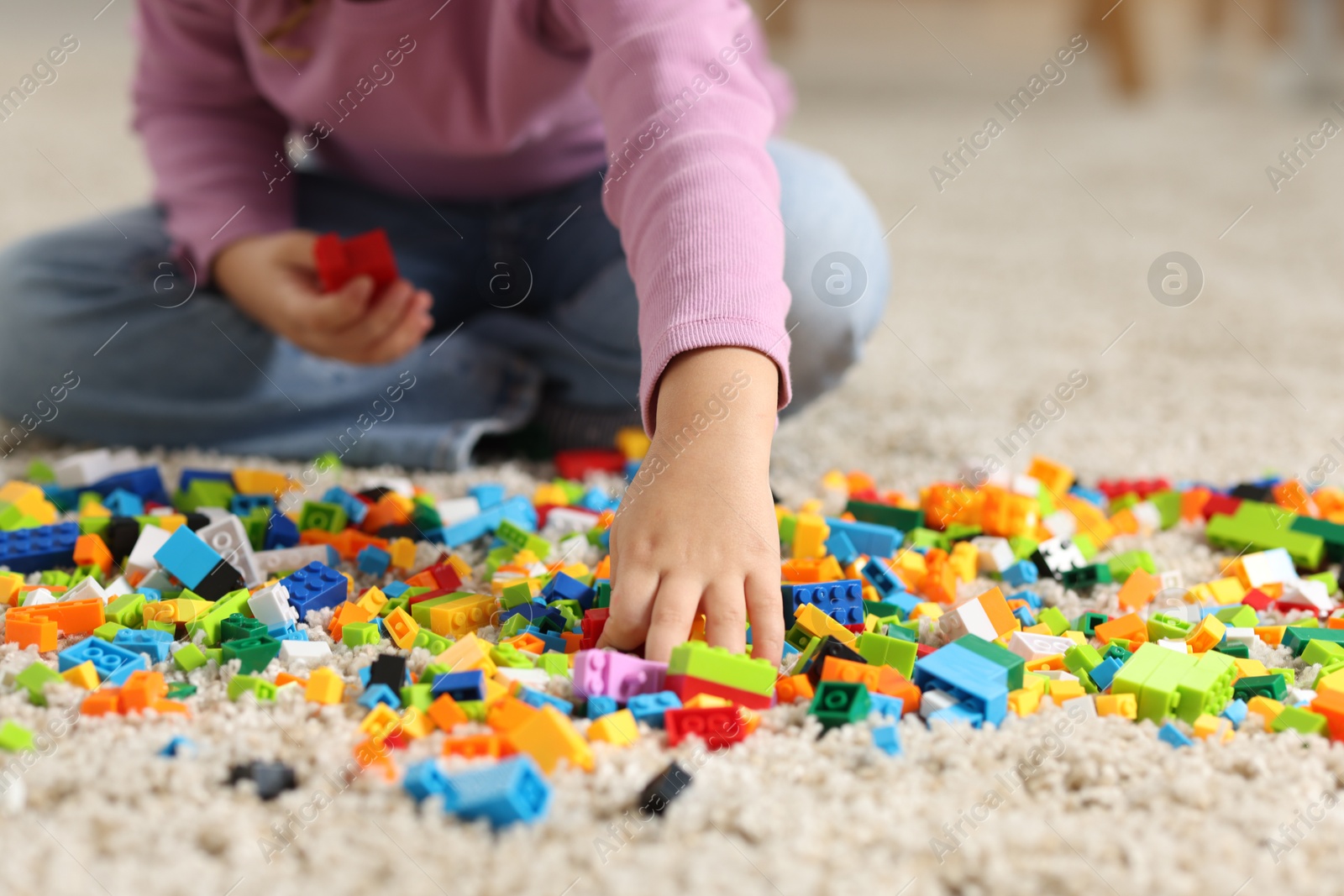 Photo of Girl playing with building blocks on floor at home, closeup