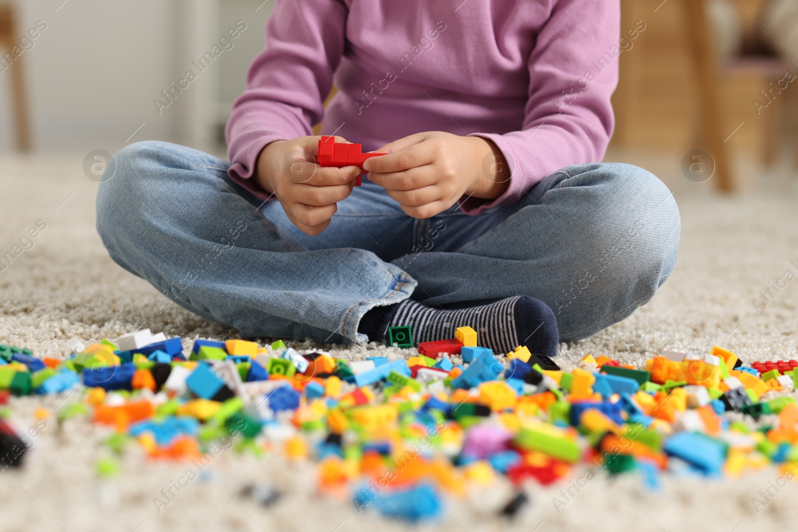 Photo of Girl playing with building blocks on floor at home, closeup