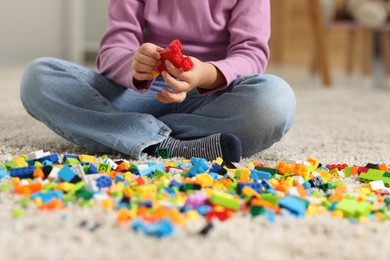 Photo of Girl playing with building blocks on floor at home, closeup