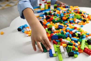 Photo of Girl playing with building blocks at white table indoors, closeup