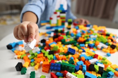 Photo of Girl playing with building blocks at white table indoors, closeup. Selective focus