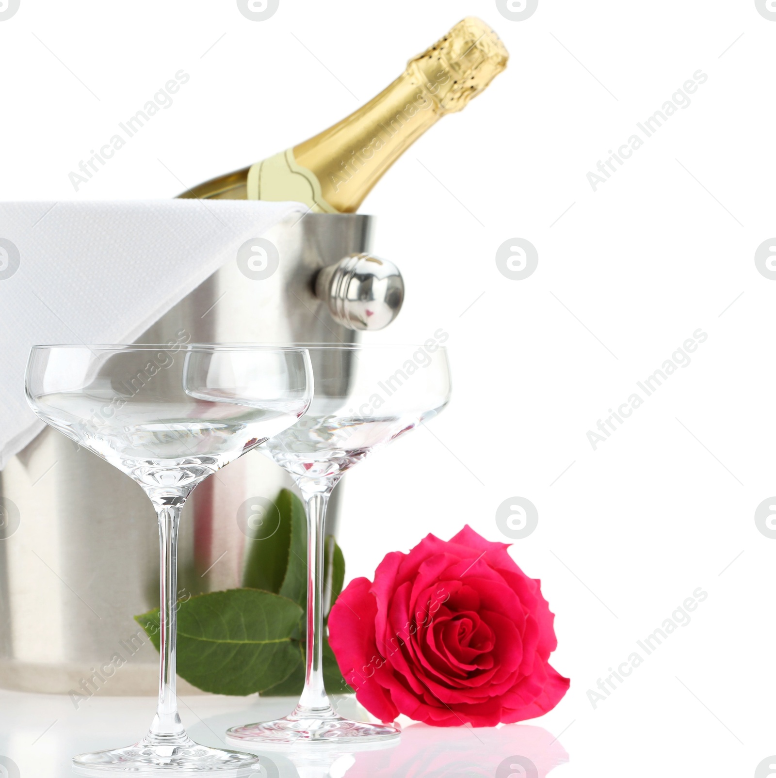 Photo of Bottle of champagne in ice bucket, beautiful rose and empty glasses isolated on white