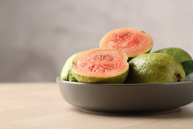 Photo of Fresh guava fruits in bowl on wooden table against blurred grey background, closeup