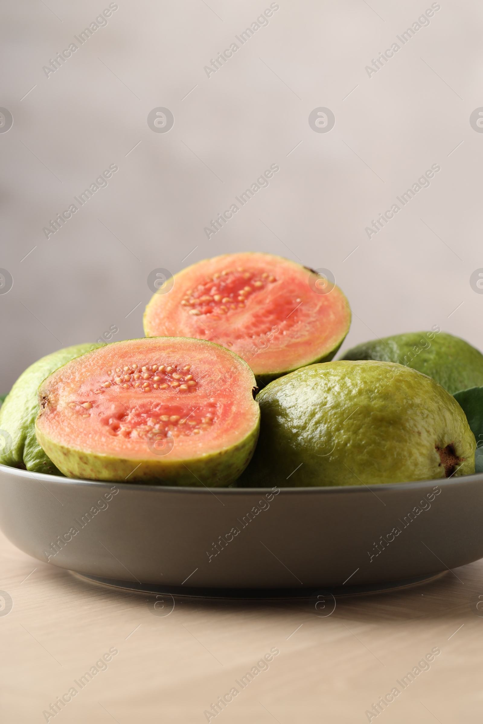 Photo of Fresh guava fruits in bowl on wooden table against blurred grey background