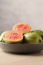 Photo of Fresh guava fruits in bowl on wooden table against blurred grey background