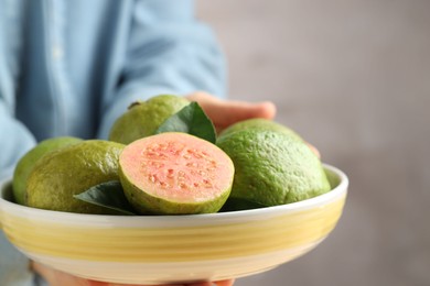 Photo of Woman with bowl of fresh guava fruits on blurred grey background, closeup