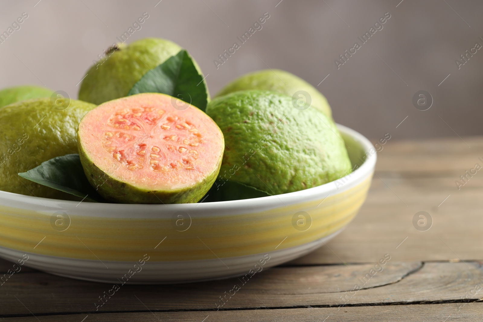 Photo of Fresh guava fruits in bowl on wooden table against blurred grey background, closeup