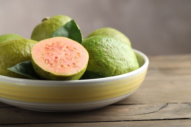 Photo of Fresh guava fruits in bowl on wooden table against blurred grey background, closeup