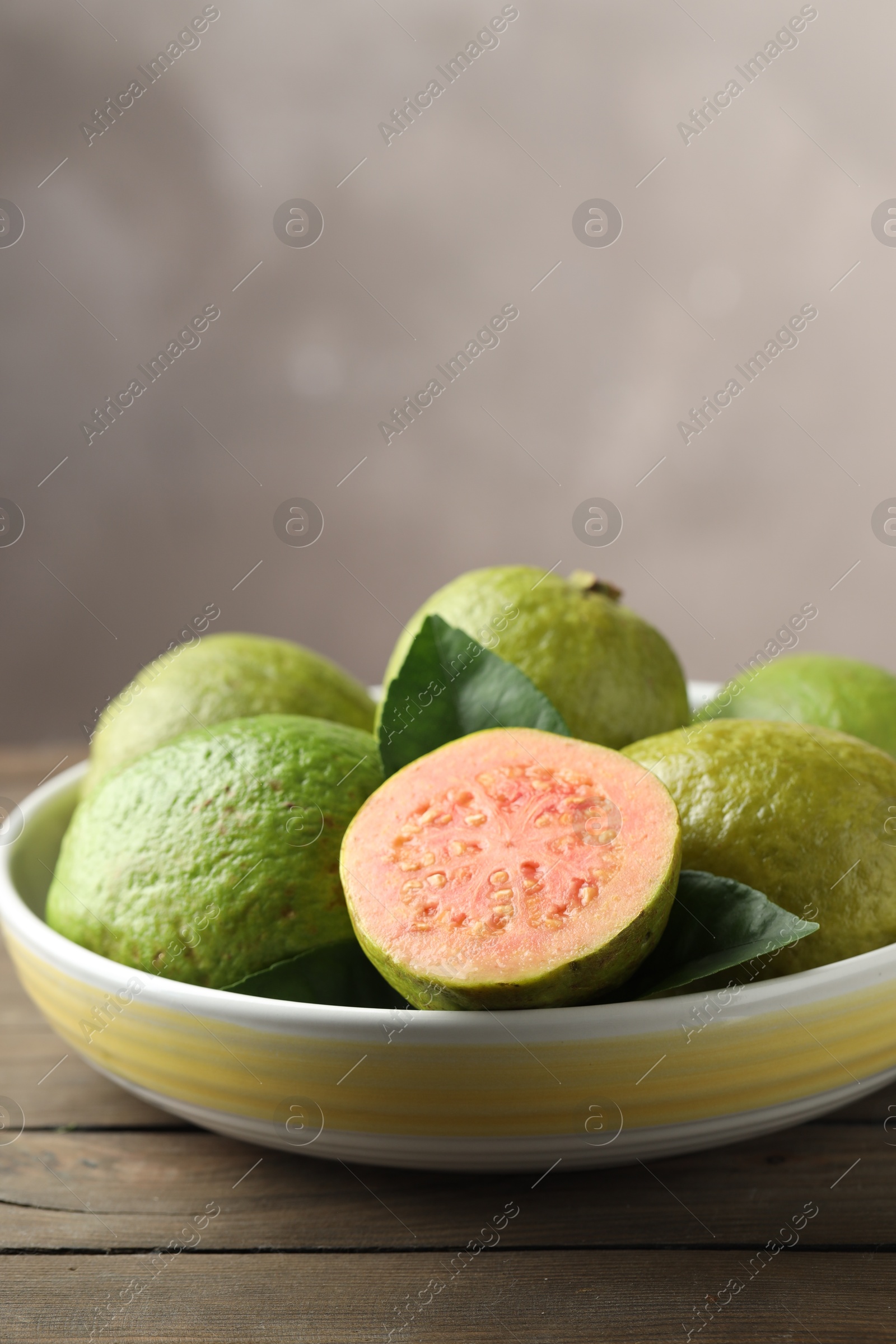 Photo of Fresh guava fruits in bowl on wooden table against blurred grey background, closeup