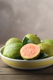 Photo of Fresh guava fruits in bowl on wooden table against blurred grey background, closeup