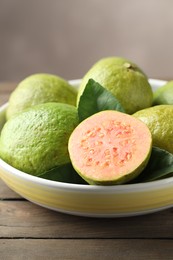 Photo of Fresh guava fruits in bowl on wooden table against blurred grey background, closeup