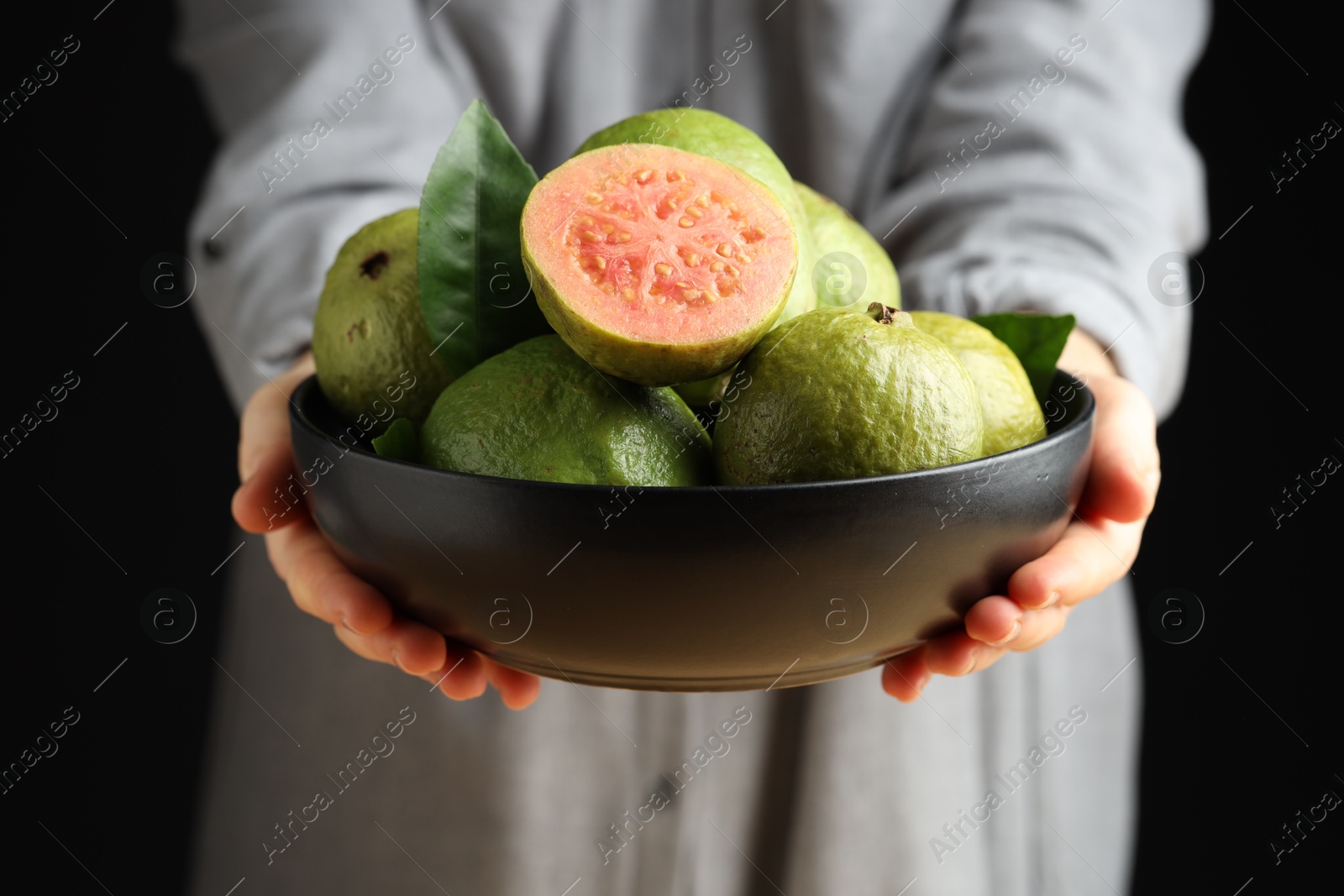 Photo of Woman with bowl of fresh guava fruits on black background, closeup