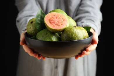 Photo of Woman with bowl of fresh guava fruits on black background, closeup