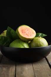 Photo of Fresh guava fruits in bowl on wooden table against black background, closeup